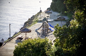 A beach with a wooden play structure, picnic tables, and thatched umbrellas.