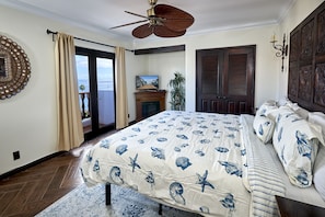 A bedroom with a large bed, a ceiling fan, a TV, and a view of the ocean through a sliding door.