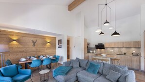 Un soggiorno moderno con un divano angolare grigio, poltrone blu e un'area da pranzo con una parete in legno e una testa di cervo appesa.