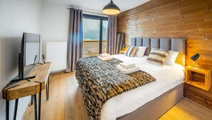 Una camera d'albergo moderna con un letto grande, una testiera in legno e un televisore su un tavolo di legno.