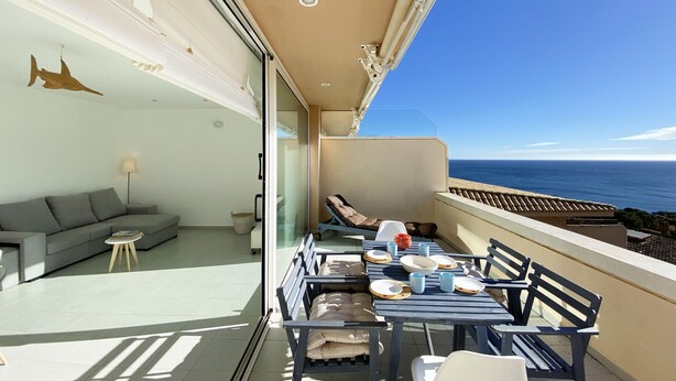 Un balcón con comedor, sofá y lámpara con vista al mar.