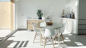 Una cocina moderna con una mesa de vidrio, sillas blancas, un armario de madera y una planta de cactus.