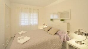 Un dormitorio con cama, escritorio, lámpara, espejo y ventana con cortinas.