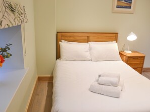 Un lit bien fait, avec du linge de lit blanc et des oreillers, une tête de lit en bois, une lampe de chevet et un tableau encadré au mur.