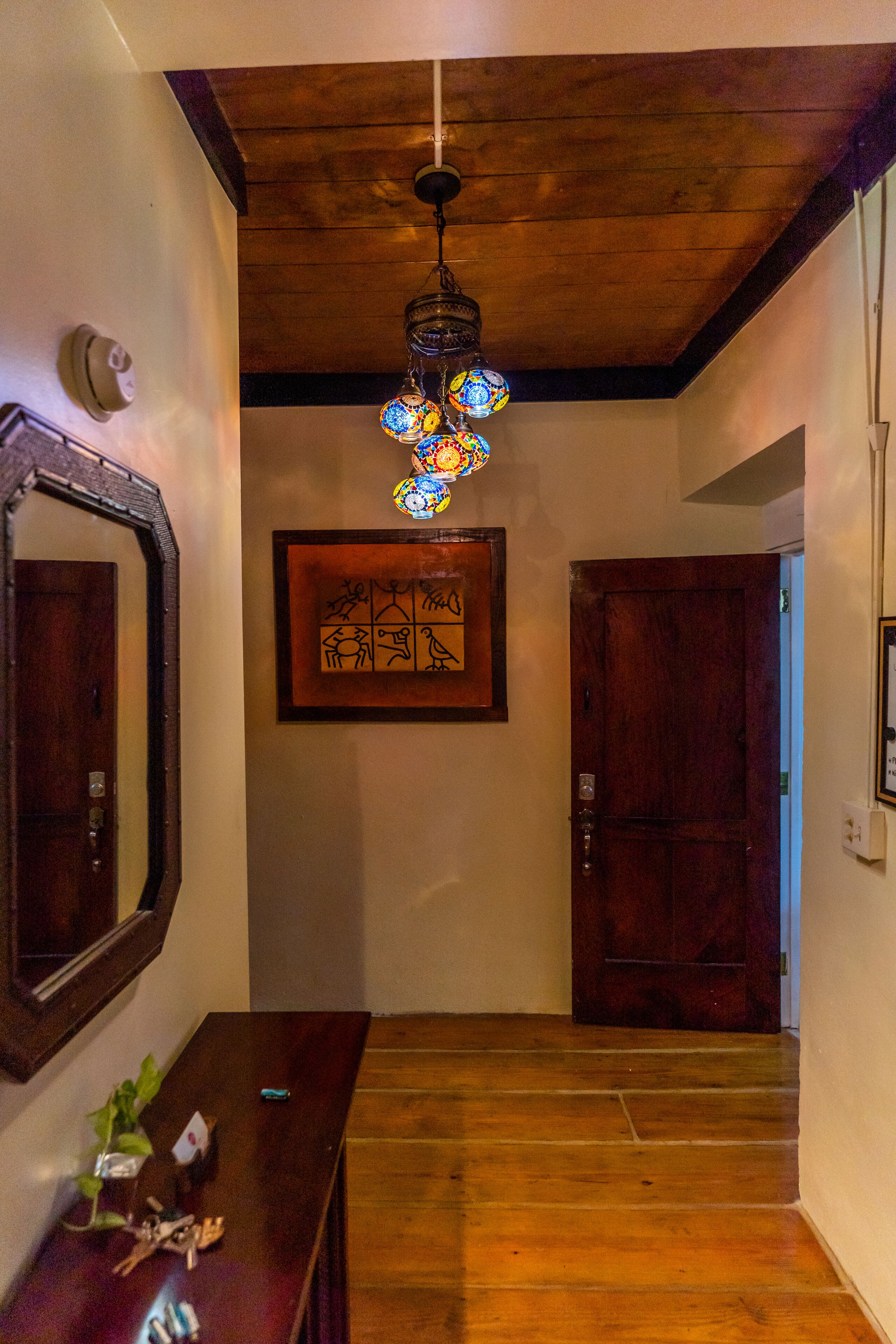 Un pasillo con piso de madera, un candelabro, una obra de arte enmarcada y una puerta.