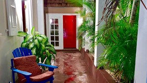 Un couloir étroit avec une porte rouge, une chaise bleue et des plantes en pot.