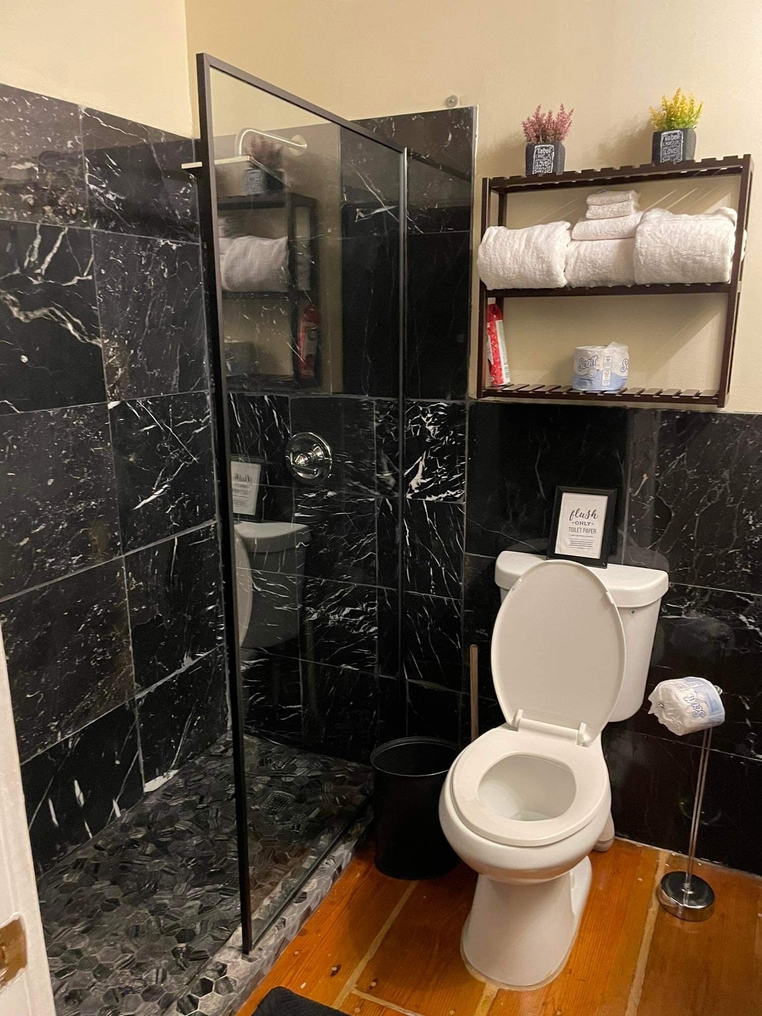 Kylpyhuoneessa on lasiseinällä varustettu suihku, wc ja hyllyjä, joilla on pyyhkeitä ja hygieniatuotteita.