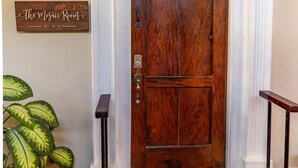 Une porte en bois avec un paillasson, une enseigne fixée au mur et une plante en pot.