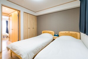 A bedroom with two single beds, wooden headboards, a bedside table with a tissue box, and a wardrobe.