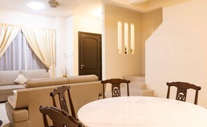 Una sala de estar con un sofá, una mesa de comedor con sillas, una puerta de madera oscura y una escalera.