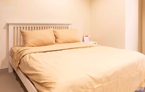 Una cama bien hecha con cabecera blanca y dos almohadas, una mesita de noche con un calendario y una pared lisa.