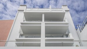 Ein modernes Gebäude mit mehreren Balkonen und großen Fenstern vor einem teils bewölkten Himmel.