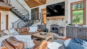 A spacious living area with a stone fireplace, leather furniture, a large flat-screen TV, and a staircase with wooden railings. - Relax in the most beautiful, secluded setting Sonoma County has to offer (Santa Rosa)