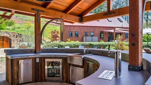A modern outdoor kitchen with a curved countertop, built-in appliances, and a stone wall backdrop. - Relax in the most beautiful, secluded setting Sonoma County has to offer (Santa Rosa)