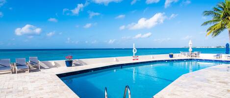 A pool area with clear blue water, lounge chairs, and a view of the ocean.