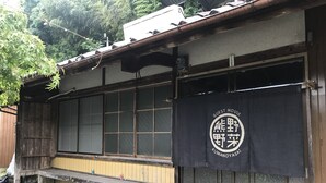 A traditional Japanese building with a wooden exterior, a black banner with white text, and a wooden bench outside. - Guest House Kumanoyasai (Tanabe)