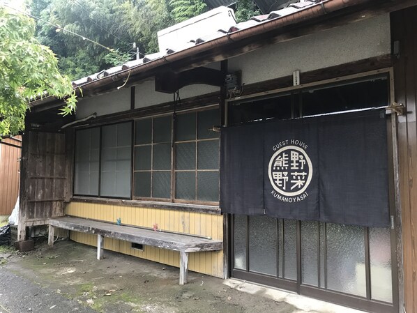 A traditional Japanese building with a wooden exterior, a black banner with white text, and a wooden bench outside. - Guest House Kumanoyasai (Tanabe)