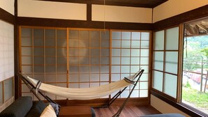 A room with a hammock, dark sofas, and a view through large windows. - Guest House Kumanoyasai (Tanabe)