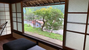 A room with tatami flooring, a low table with a notebook, pen, and clock, and a view of a tree-lined street through a shoji screen. - Guest House Kumanoyasai (Tanabe)