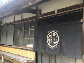 A traditional Japanese building with a wooden exterior and a black banner displaying the name "Kumanoyasai" and "Guest House". - Guest House Kumanoyasai (Tanabe)