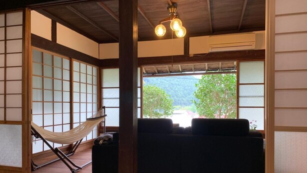 A traditional Japanese room with tatami flooring, a low wooden table, a sofa, and a hammock. - Guest House Kumanoyasai (Tanabe)