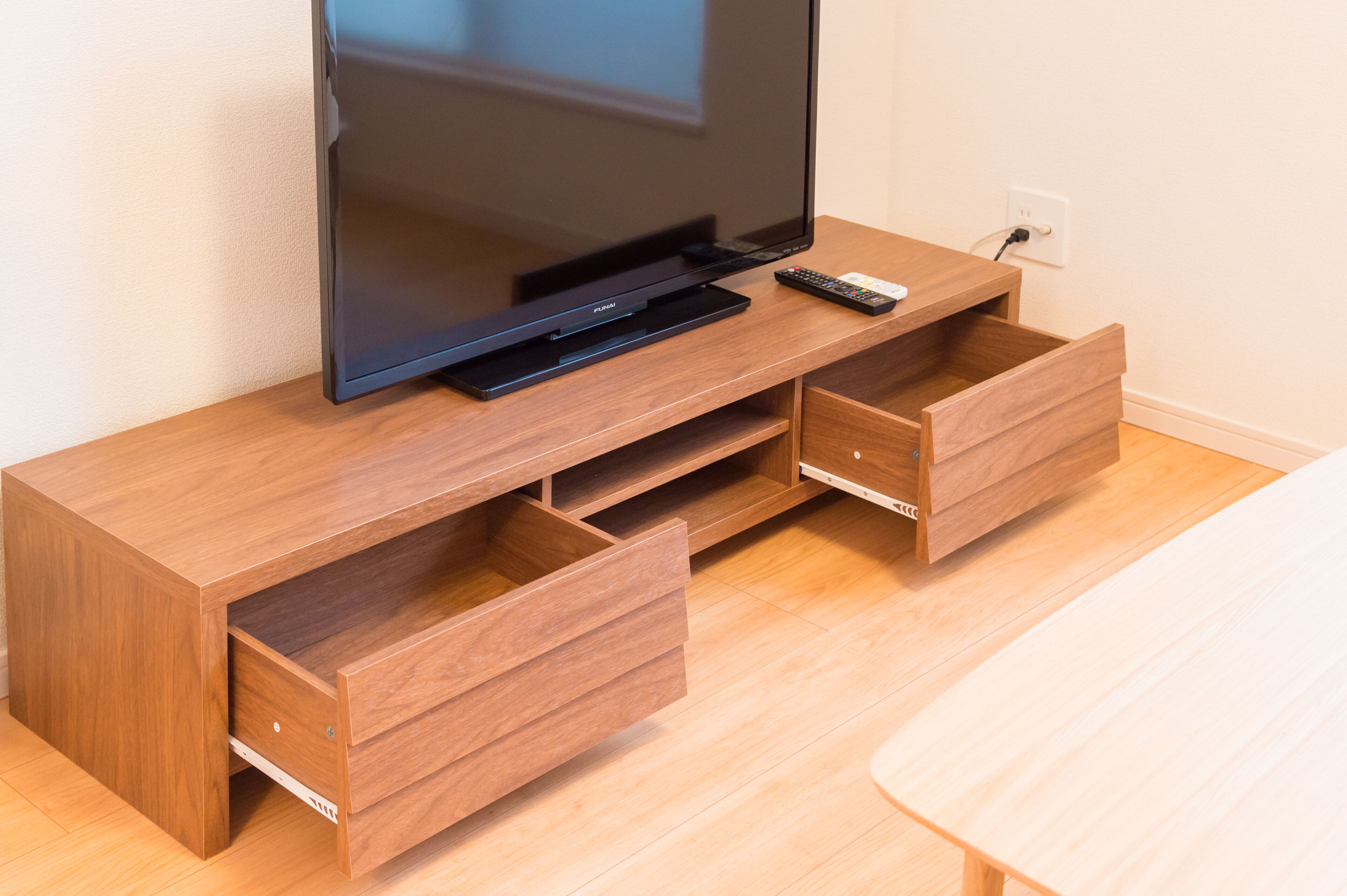 A wooden entertainment center with a flat-screen TV, remote control, and two drawers.