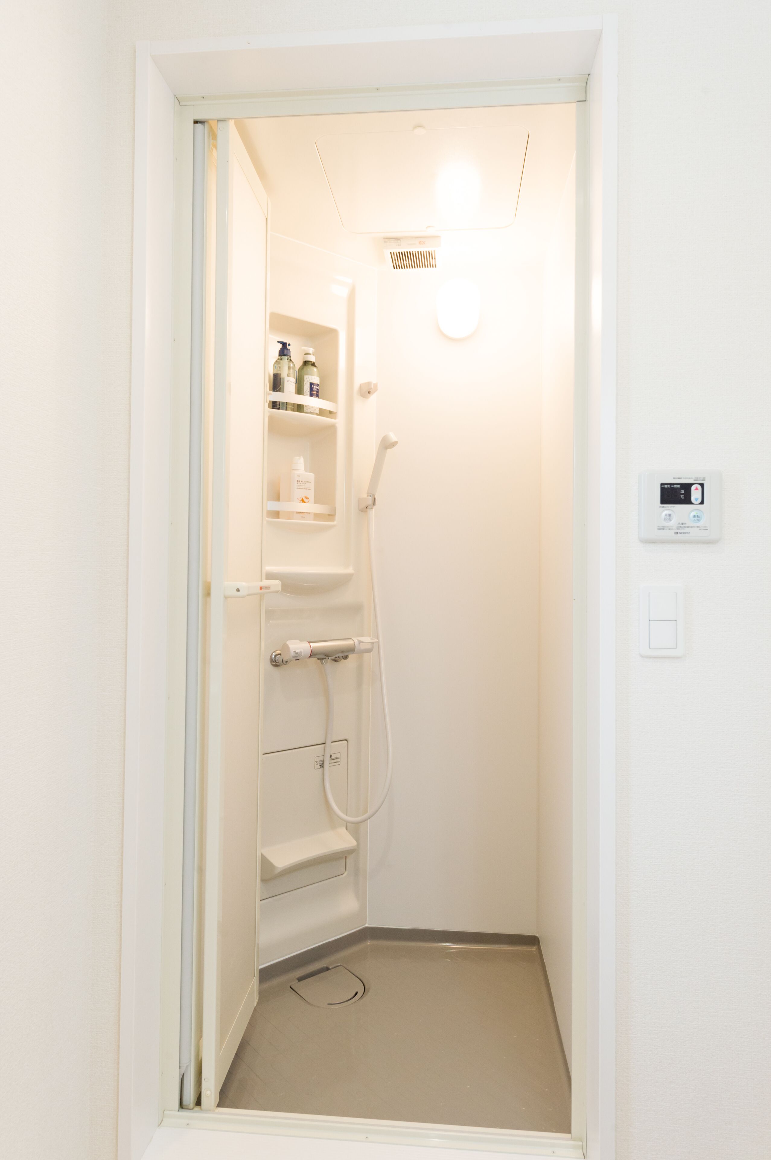A small, white bathroom with a shower, a toilet, and a shelf with toiletries.