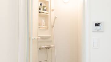 A small, white bathroom with a shower, a toilet, and a shelf with toiletries.