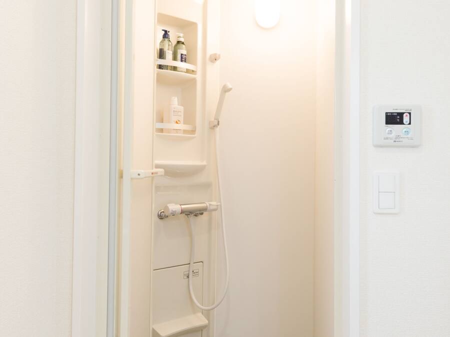 A small, white bathroom with a shower, a toilet, and a shelf with toiletries.
