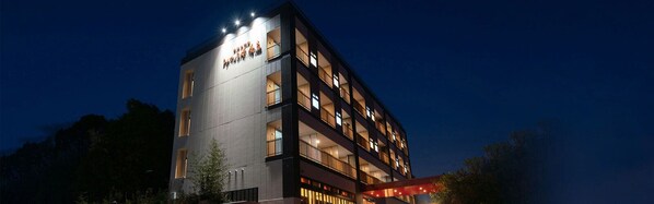 A multi-story hotel with a modern design, featuring balconies on each floor and a prominent entrance with a red awning.