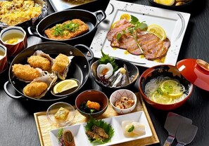 A variety of dishes including fried items, sashimi, and a bowl of noodles with lemon slices.