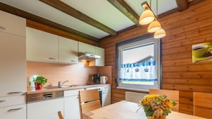 Una cocina moderna con vigas de madera, armarios blancos y una zona de comedor con una mesa y sillas de madera.