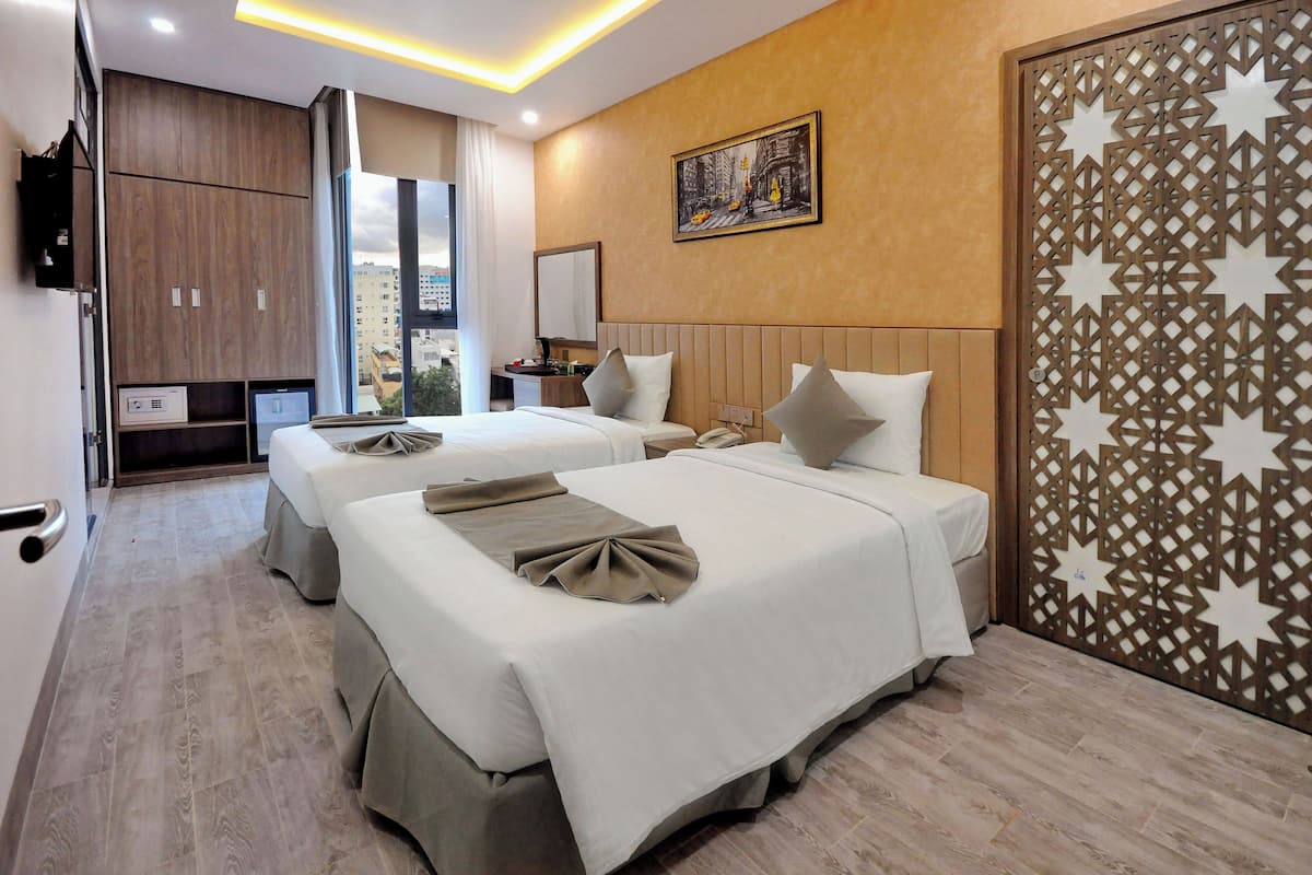 A hotel room with two beds, a large window, a desk, and a decorative partition.