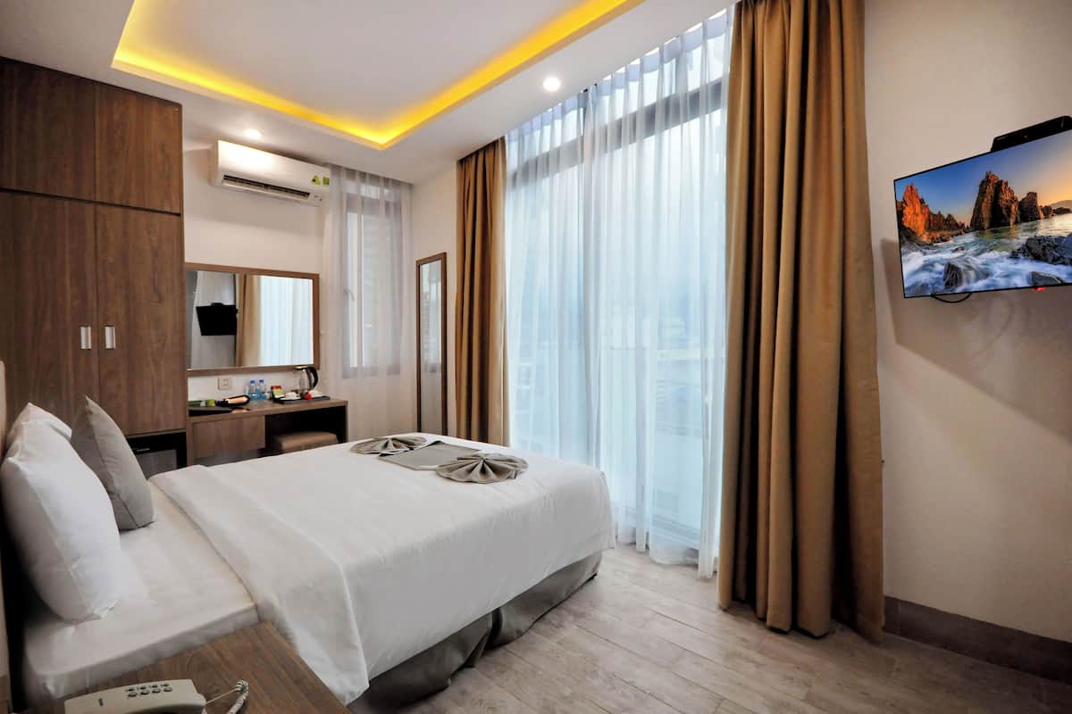 A hotel room with a bed, bedside table, and a flat-screen TV mounted on the wall.