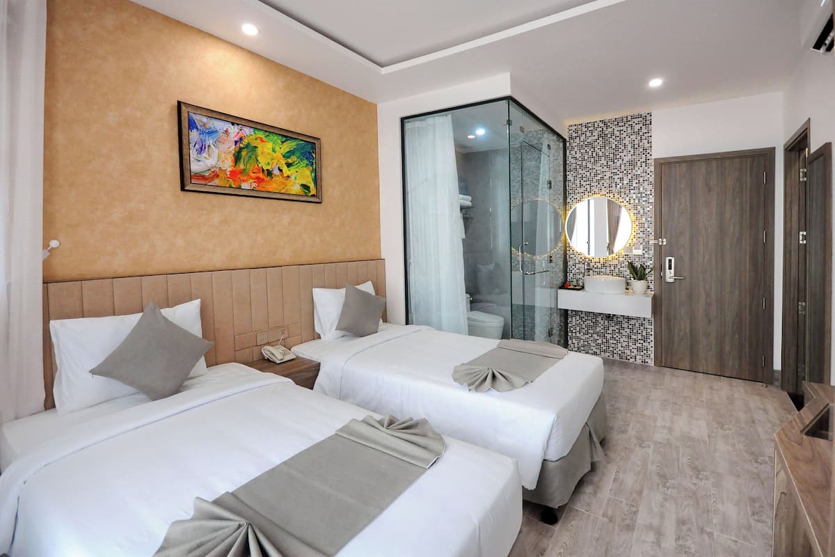A hotel room with two beds, a shower, a vanity with a mirror, and a painting on the wall.
