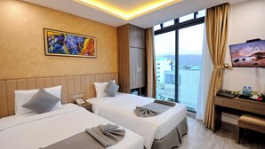 A hotel room with two beds, a desk, a TV, and a large window with a view of the city. - Angel Hotel Nha Trang (Nha Trang)