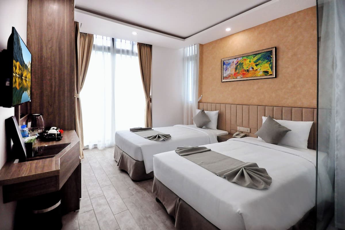 A hotel room with two beds, a TV, a desk, and a painting on the wall.