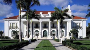 Un edificio grande y blanco con techo rojo, que presenta una fachada simétrica con columnas y arcos.