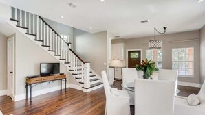 Amplia sala de estar con escalera, una mesa de comedor con sillas y un televisor sobre un mueble.