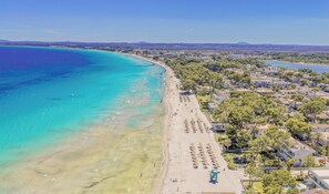 Luftaufnahme einer Küstenlandschaft mit Strand, Gebäuden und viel Grün.