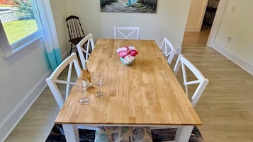 A dining room with a wooden table, white chairs, and a painting of a beach scene.