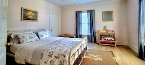 A bedroom with a bed, a bedside table, a lamp, a window with curtains, and a painting on the wall. - Immaculate Cottage in the Historic District. Quiet street, large fenced yard. (Washington)