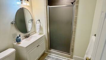 A bathroom with a toilet, sink, mirror, and shower.