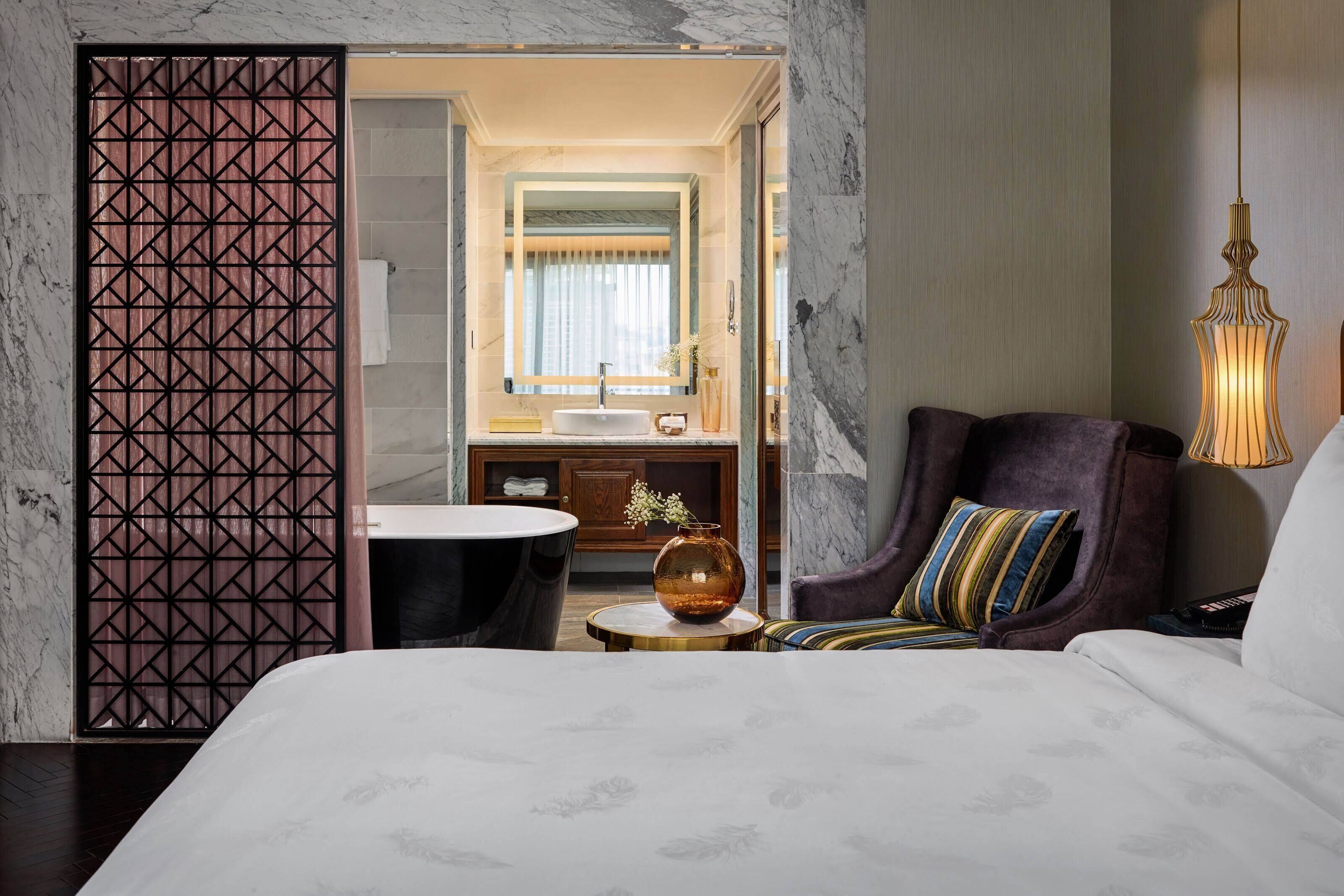 A modern hotel room with a large bed, a round table, a sofa, and a bathroom visible through an open door.