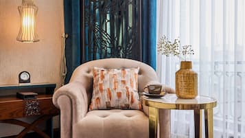 A modern living room with a plush armchair, a round table with a vase, a decorative wall panel, and a hanging light fixture.