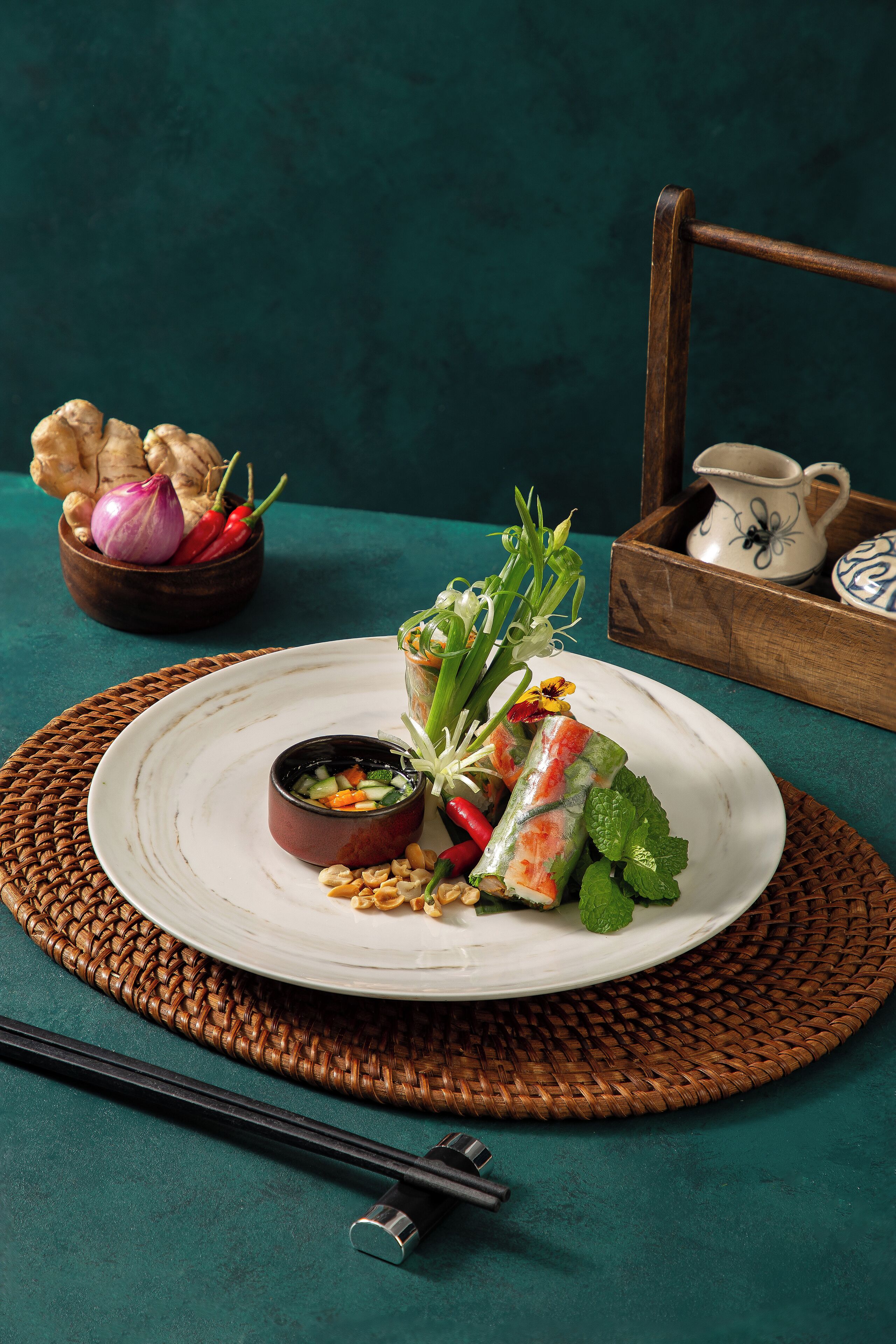 Un plato de rollitos primavera frescos con salsa para mojar, adornados con hierbas y vegetales, sobre un tapete tejido.