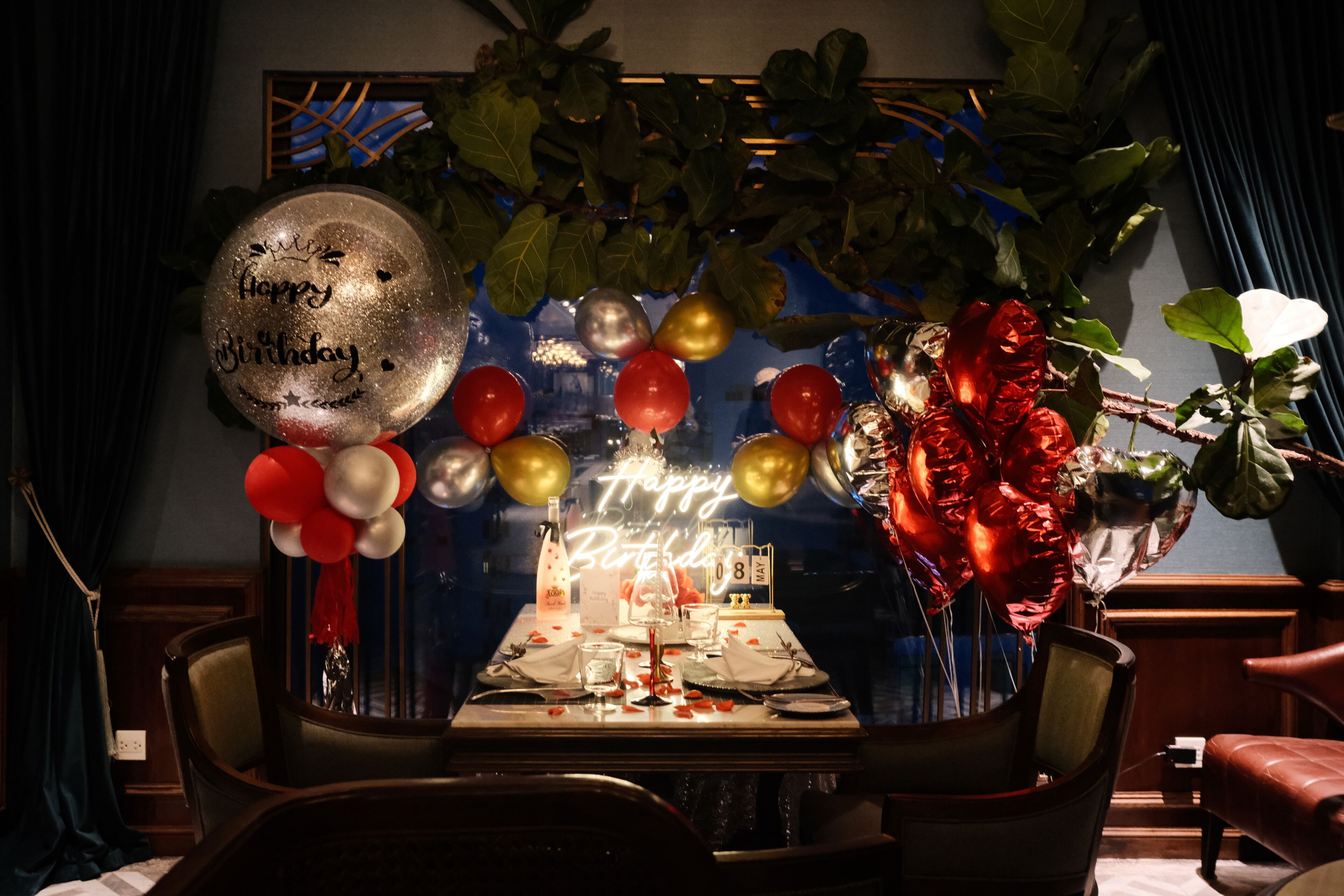 Un comedor con una mesa dispuesta para una celebración, globos y un letrero de neón.