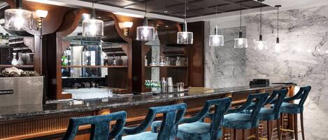 A bar area with a marble countertop, blue velvet bar stools, and pendant lighting.