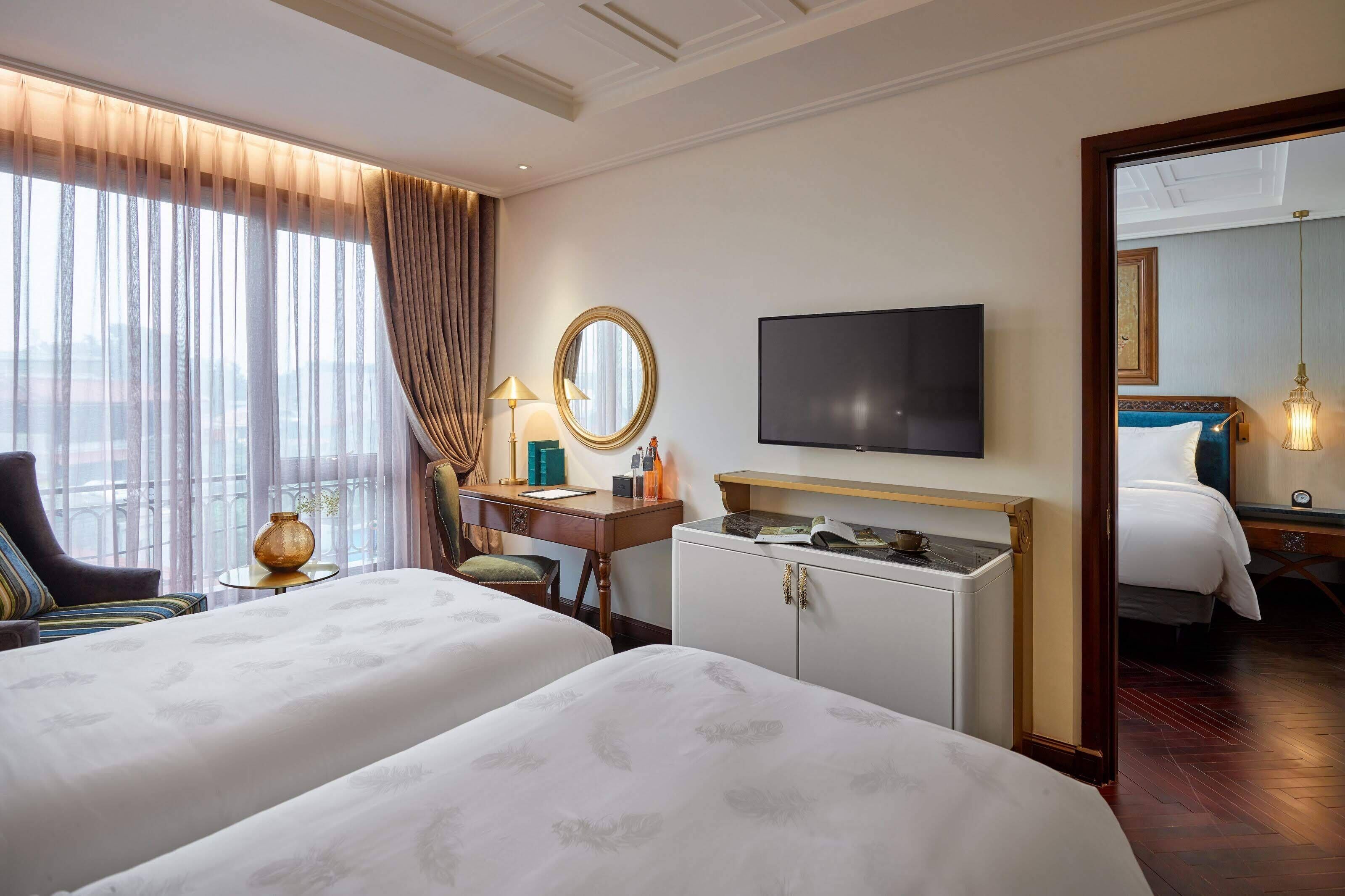 A hotel room with two beds, a desk with a lamp, a television, and a large mirror.
