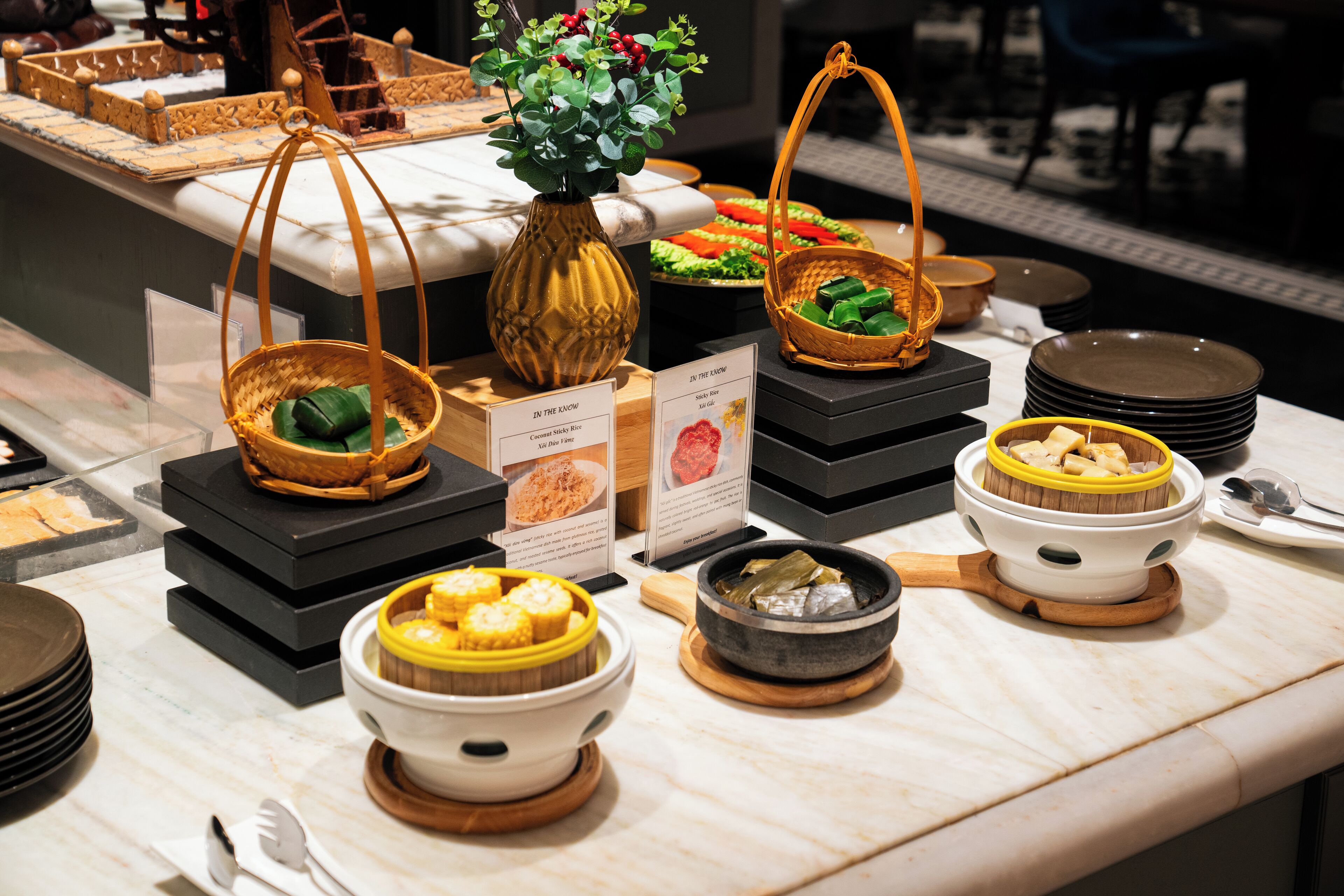 A buffet with various dishes displayed on black stands, including a basket of corn and a bowl of corn on the cob.